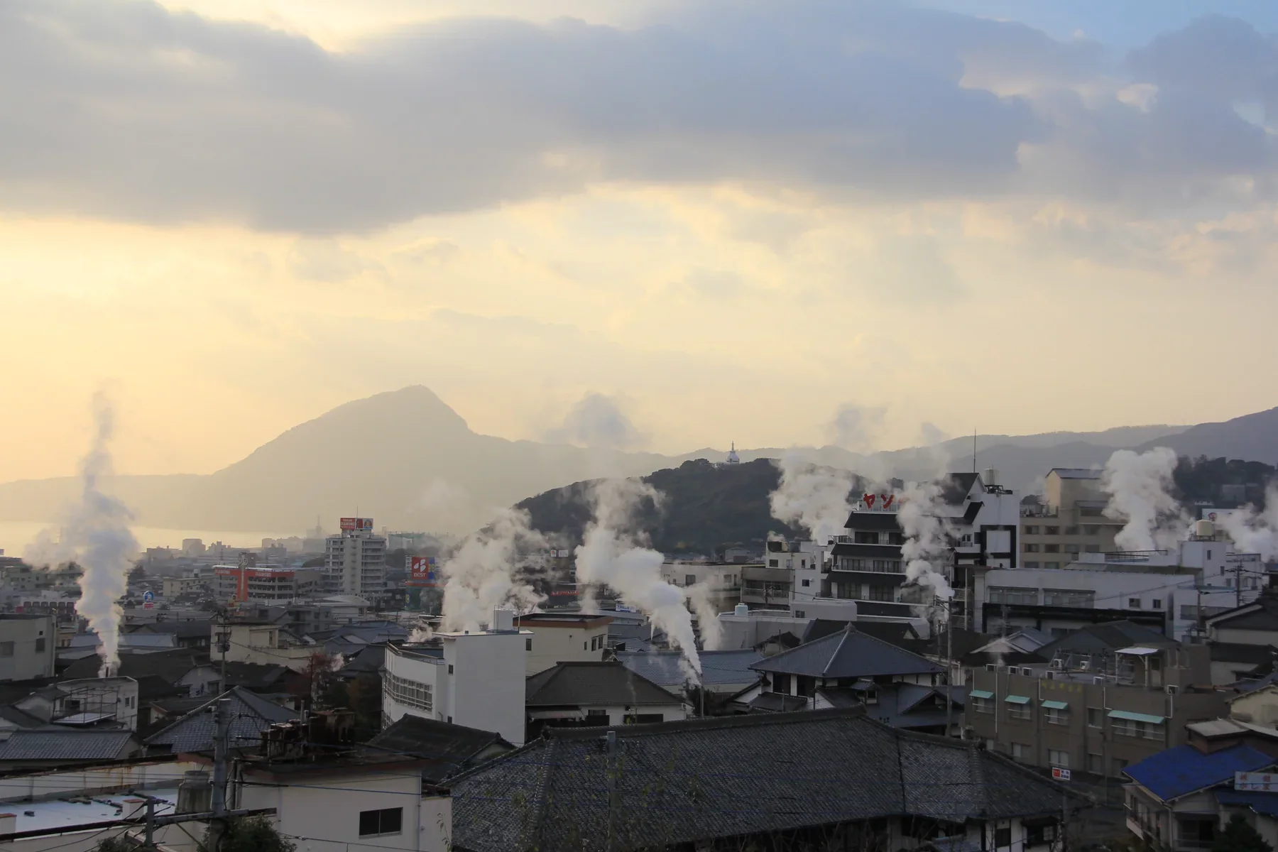 傍晚的鐵輪街區屋頂與山坡，數道溫泉蒸氣升起