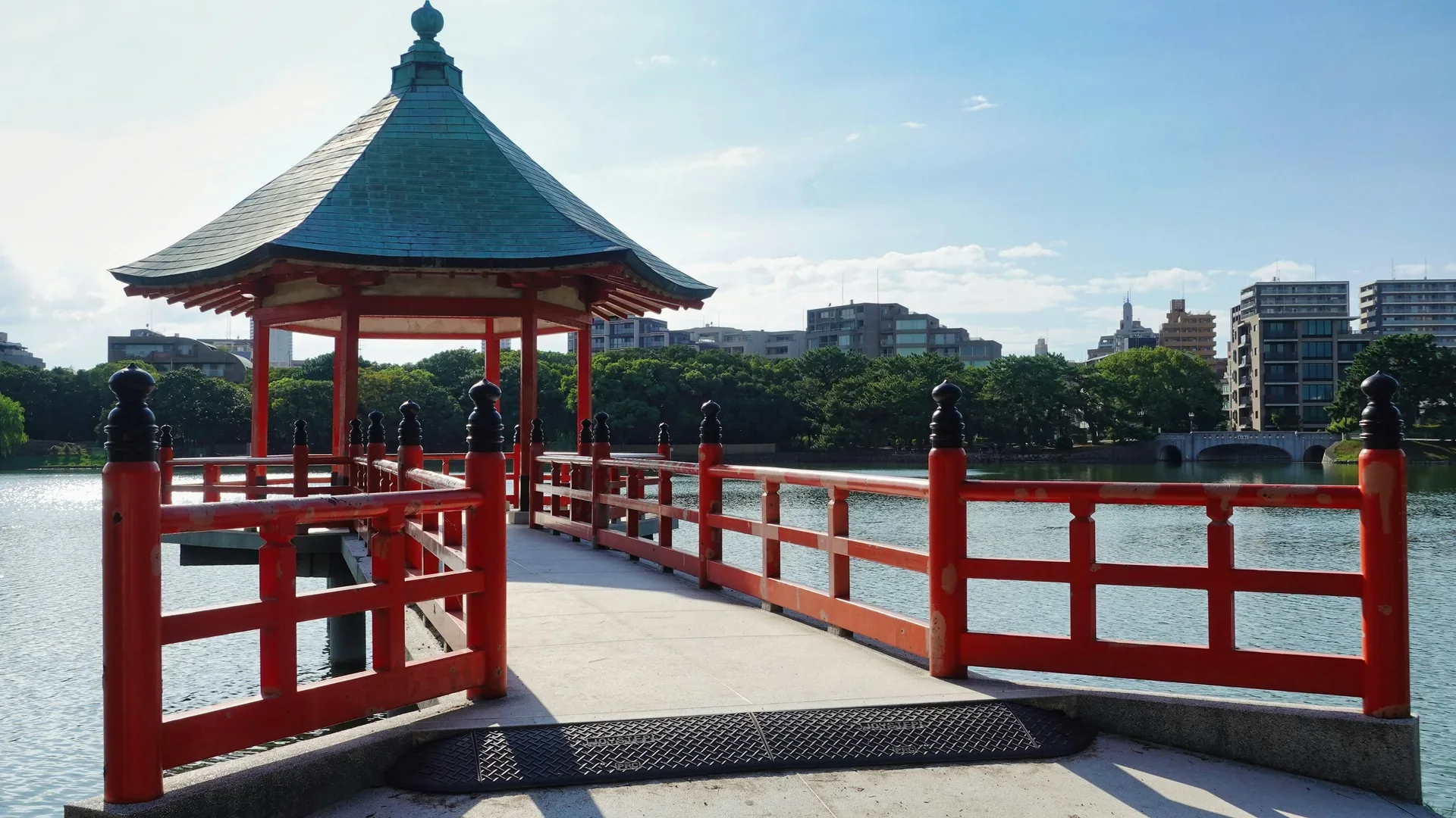 大濠公園浮見堂的紅色木造廊亭伸向湖面，遠處是福岡市區建築