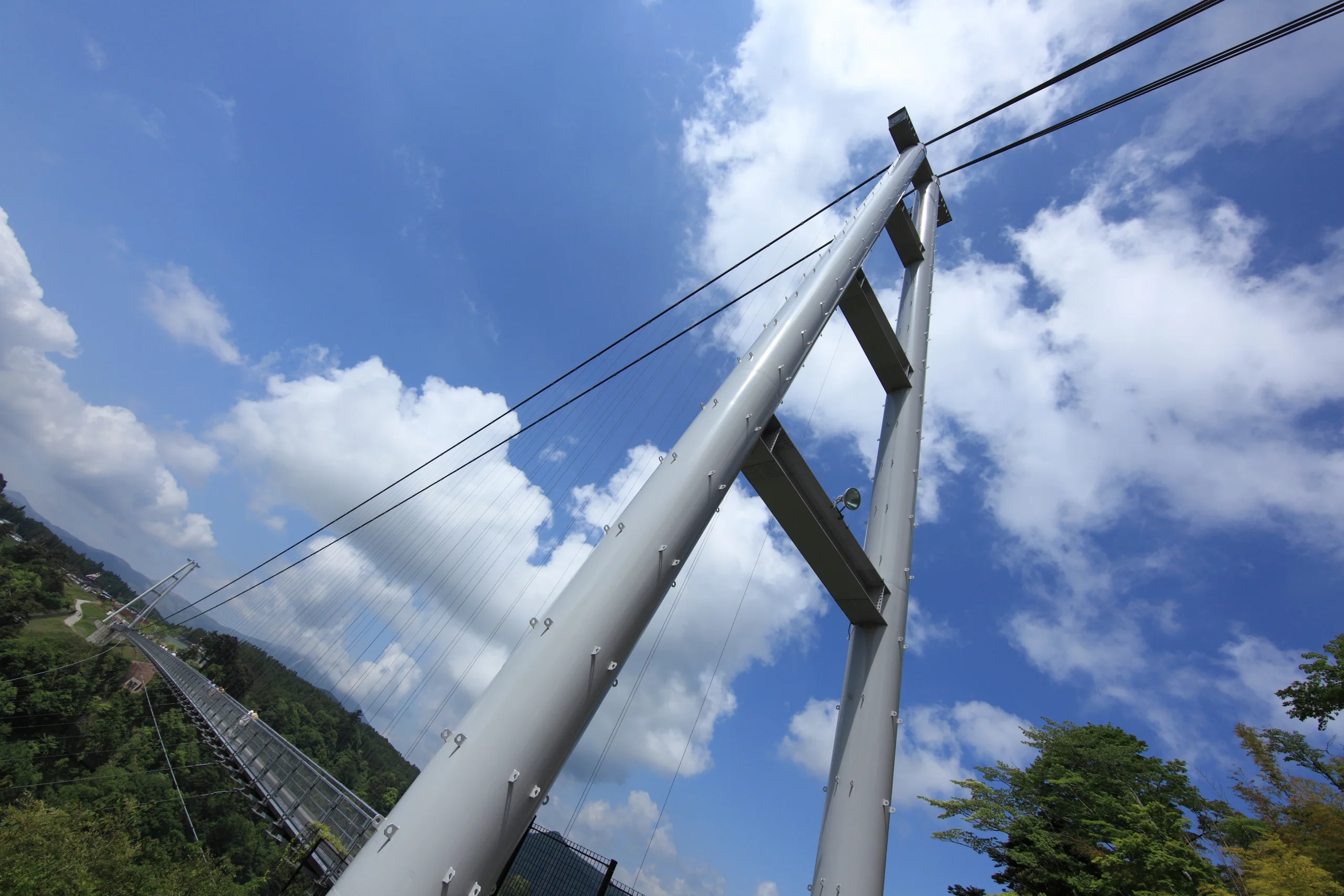 九重夢大吊橋白色主塔與鋼索由橋面仰望，遠處是九重町山谷