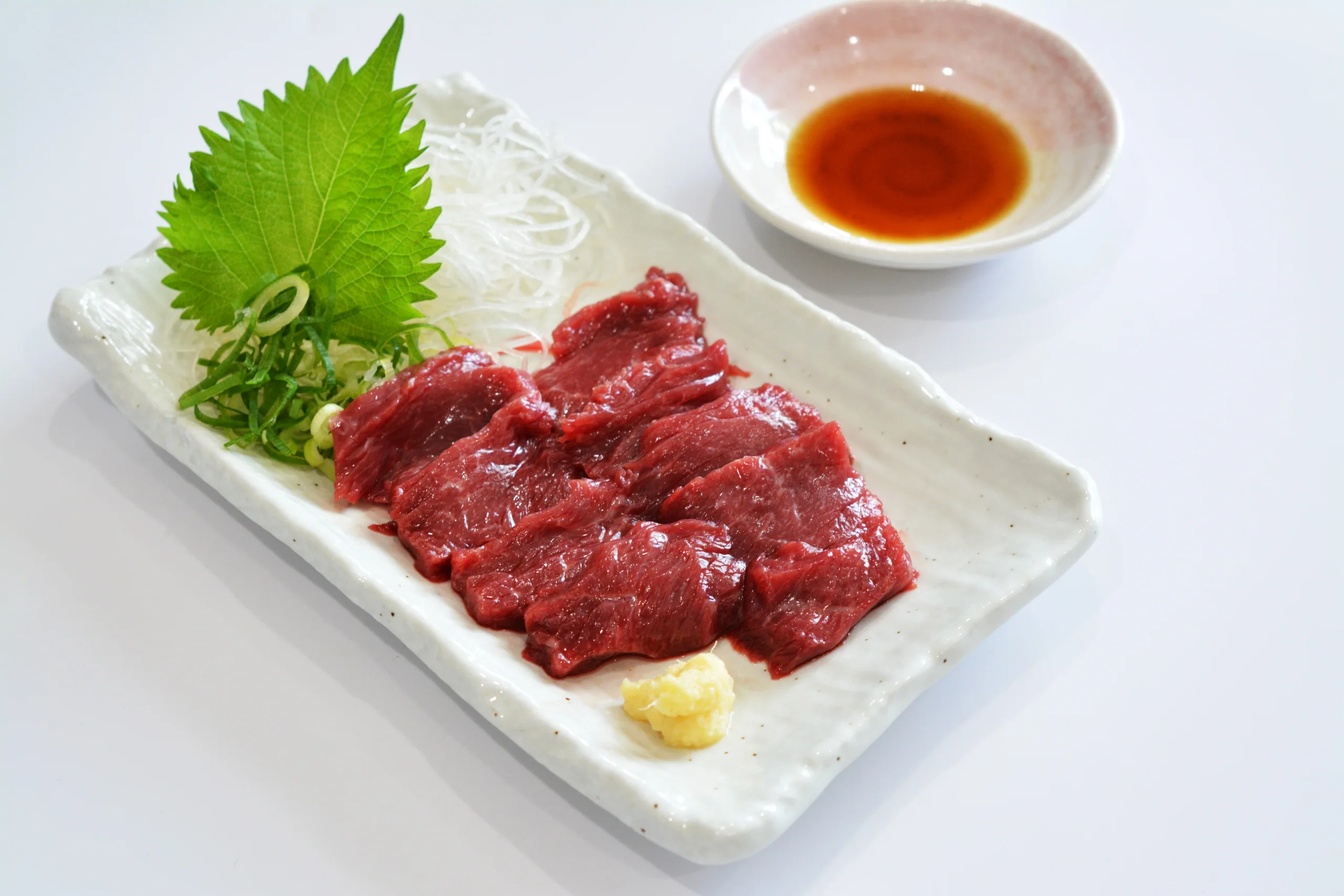 黑色長盤上的馬刺し多部位盛合せ，紅肉與脂紋切片並列