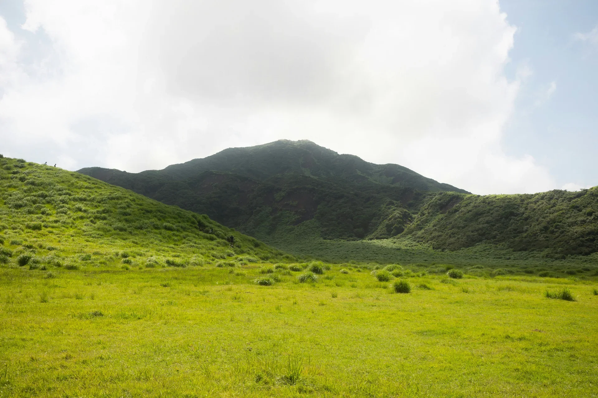 阿蘇山麓的綠色草原和山脊，近處草坡延伸至山腳