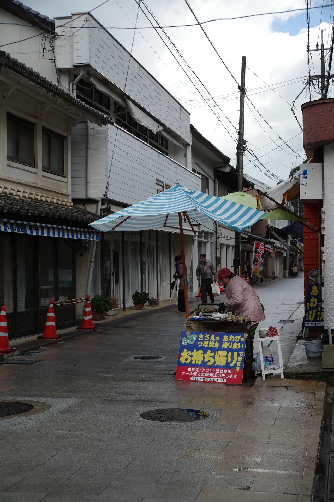 呼子朝市街道上的海產攤檔與遮陽棚，攤主和行人位於市場場景中