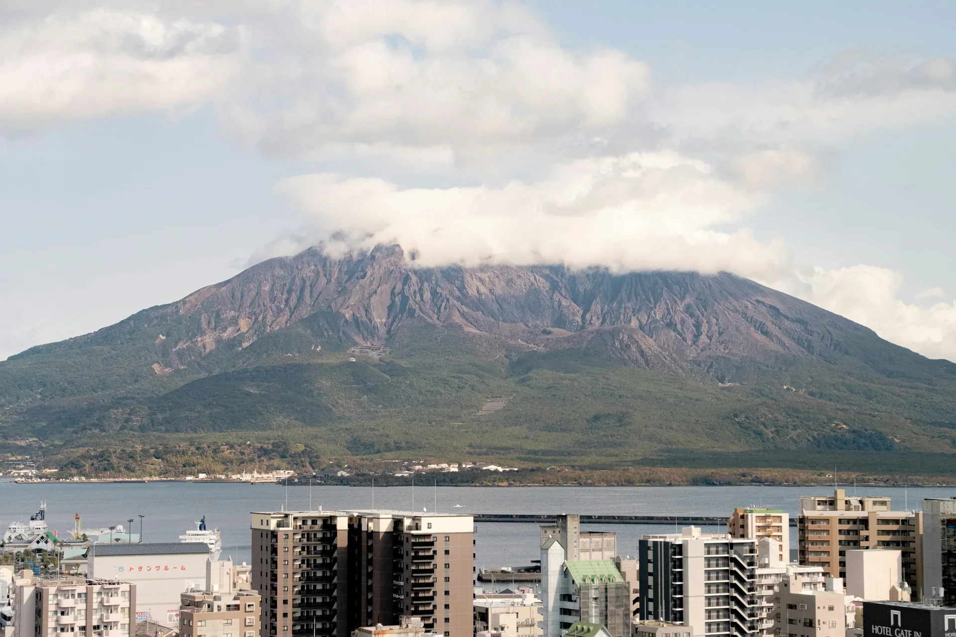 櫻島火山橫跨鹿兒島灣對望市區，前景可見海灣與城市建築