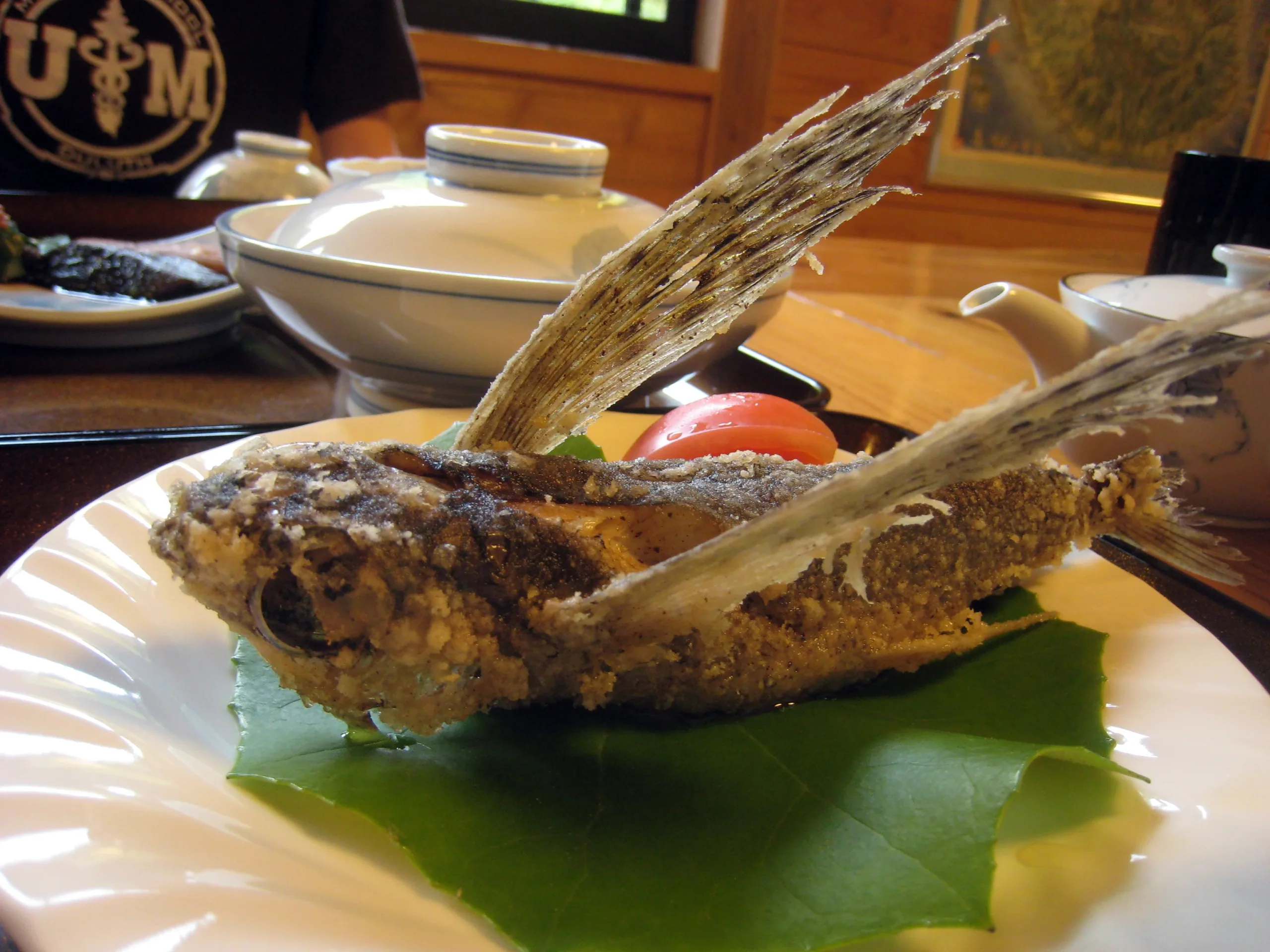 屋久島旅館晚餐中的整尾飛魚唐揚,魚鰭展開置於白色餐盤上,背景可見餐桌器皿