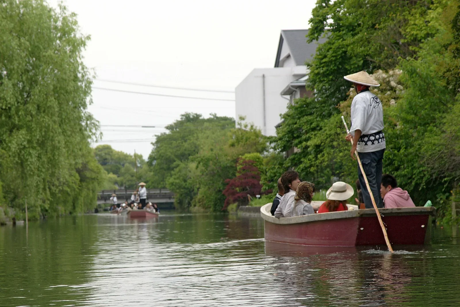 柳川川下り船頭站在船尾撐船，沿岸可見柳樹與低矮水道
